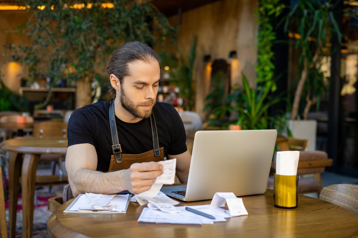 Dueño de restaurante en su establecimiento revisando facturas con la laptop y comparando si le conviene migrar a RESICO Personas Morales